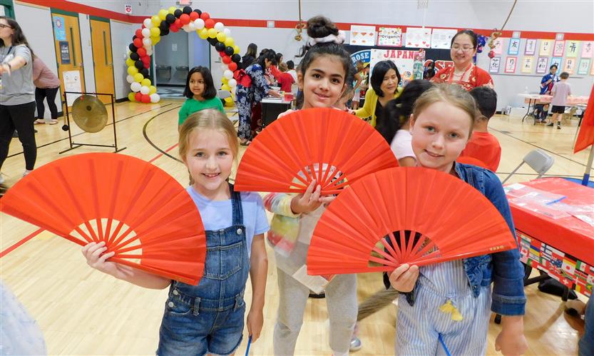 Three girls hold up red fans during International Day